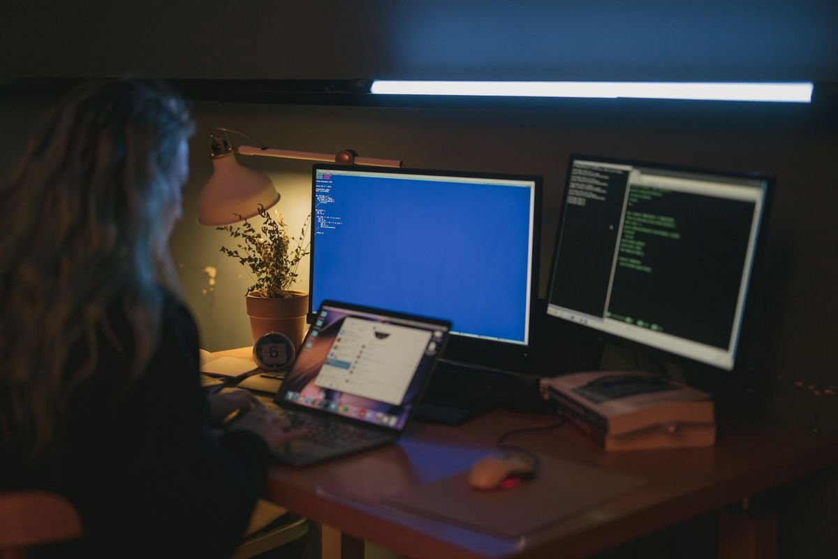 A person works across multiple monitors at a desk, reviewing security information