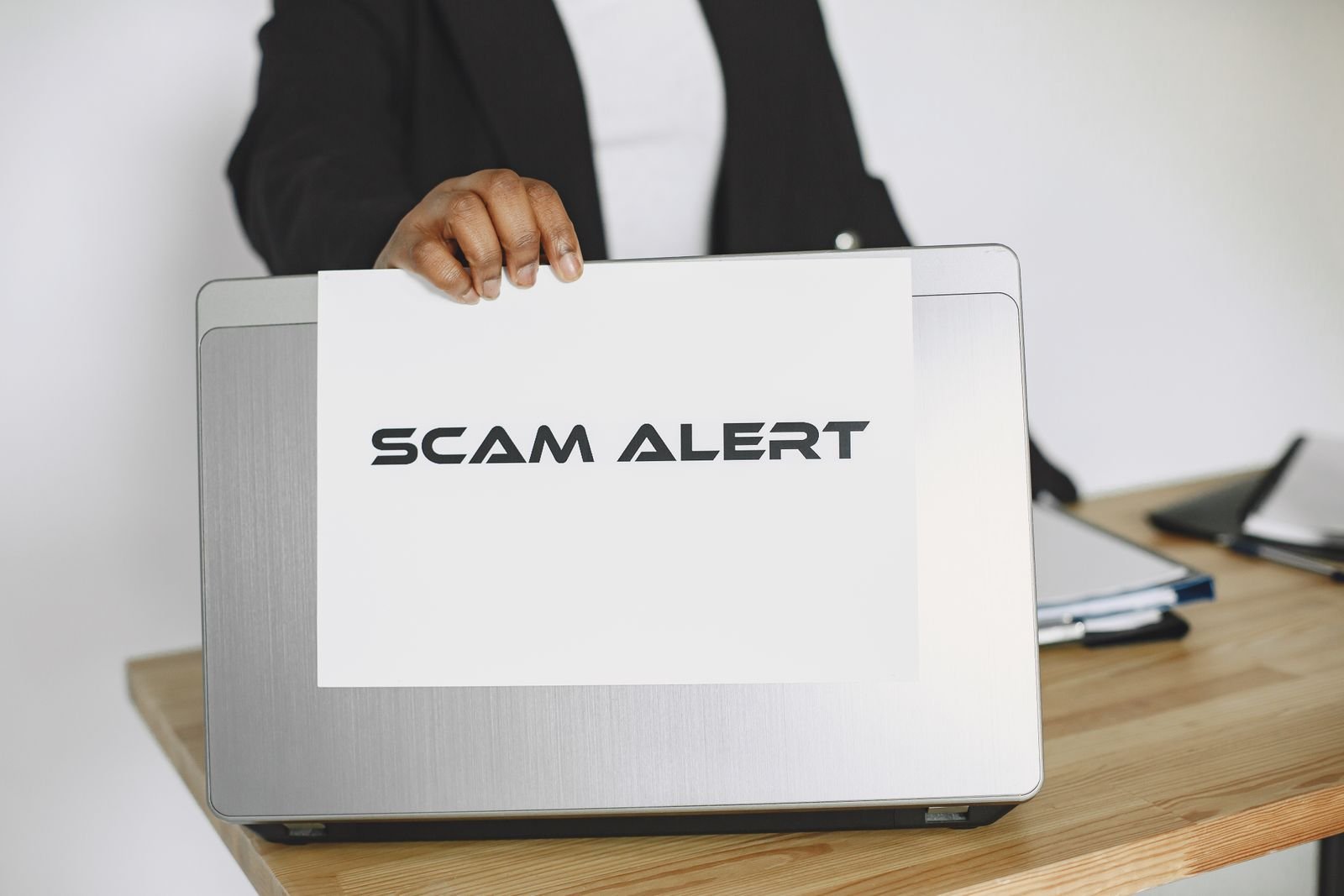 A business person holds up a scam alert sign in front of an open laptop