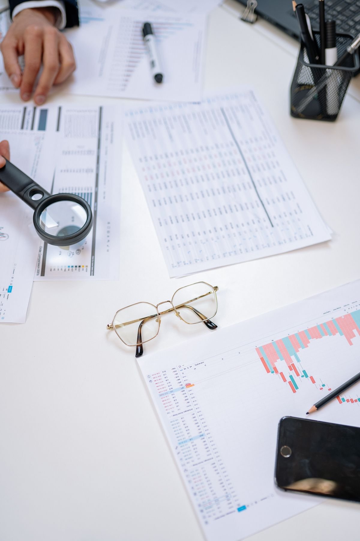 Business documents laid out with a magnifying glass, glasses and a smartphone on a desk