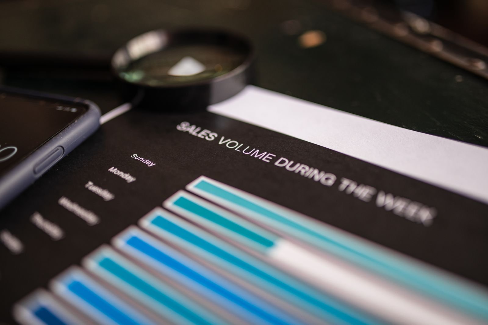 A magnifying glass and a phone rest on a weekly stats chart