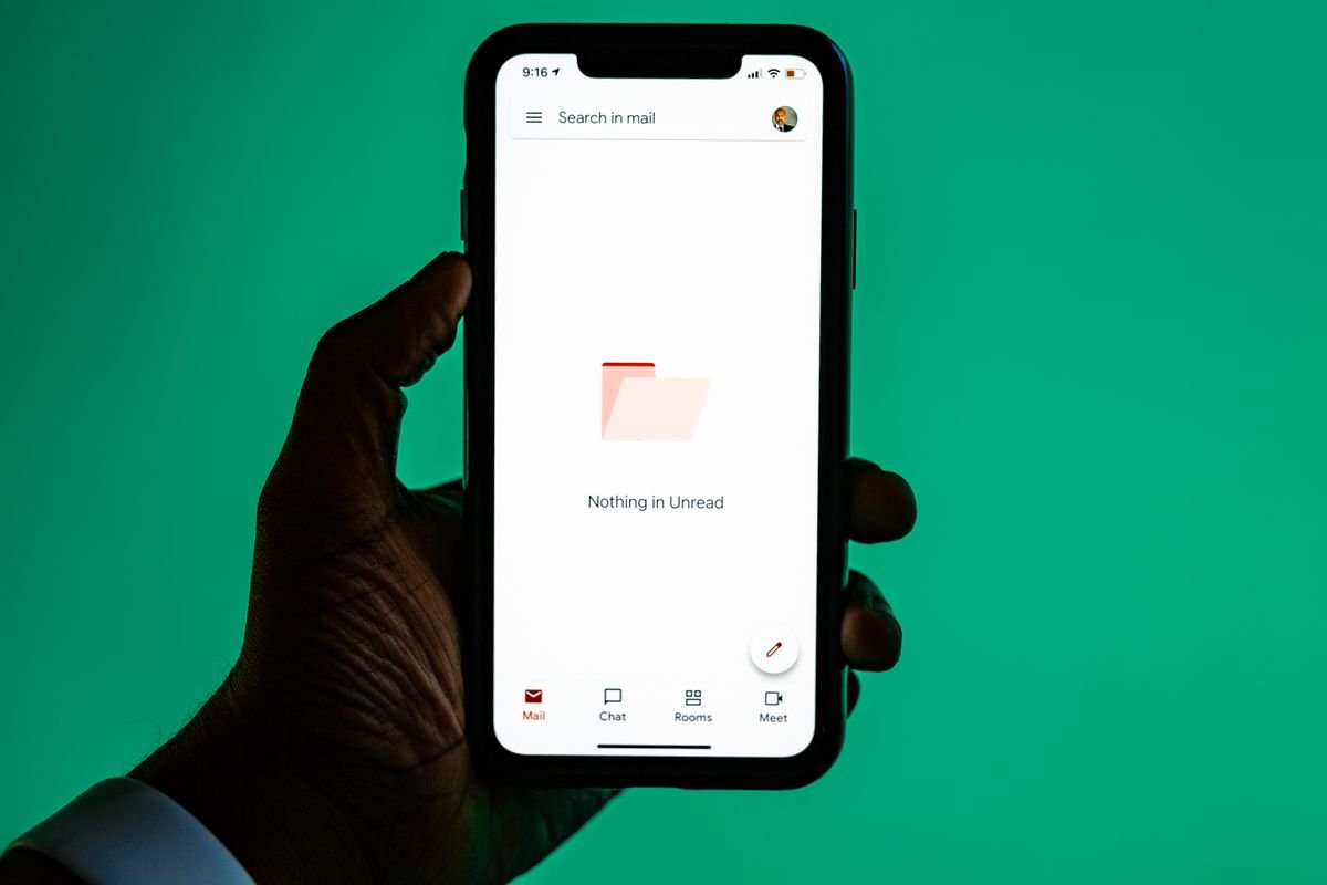 A hand holds a smartphone displaying an email app against a green background